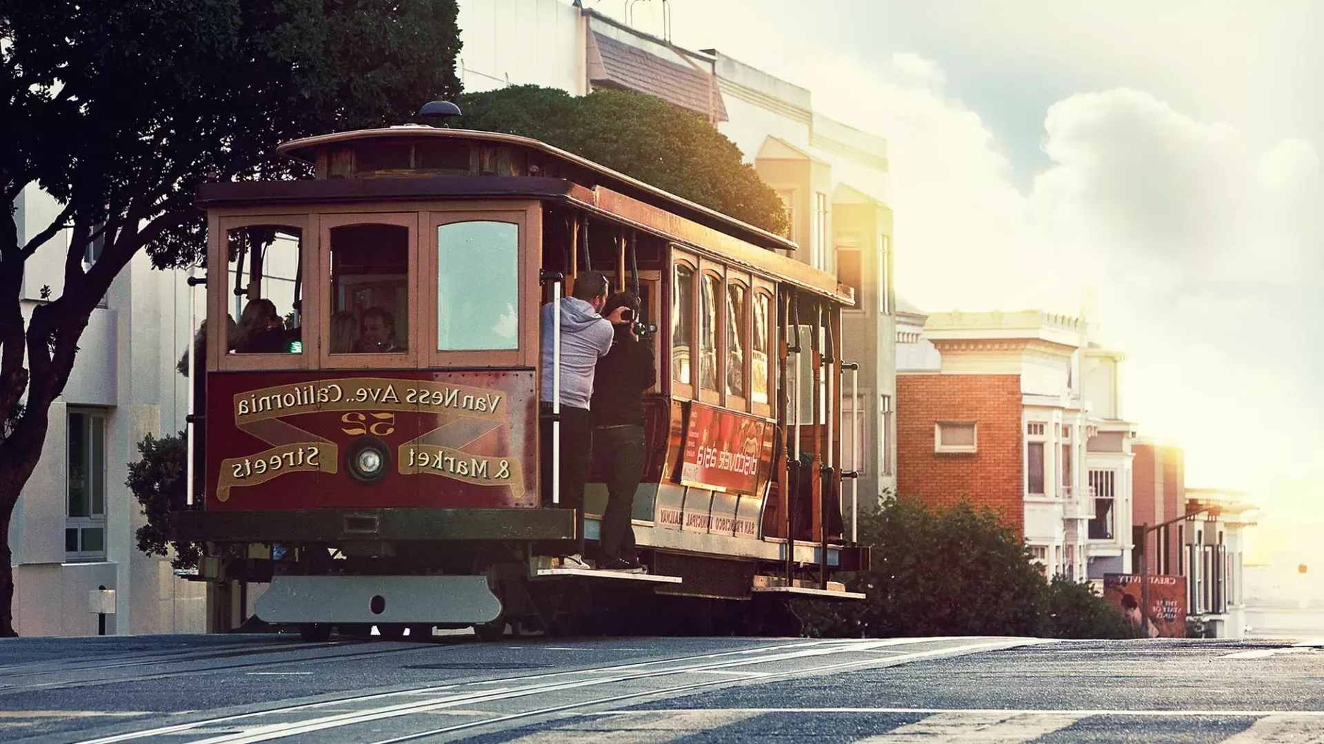 A cable car rounds a hill in San Francisco with passengers looking out the window.